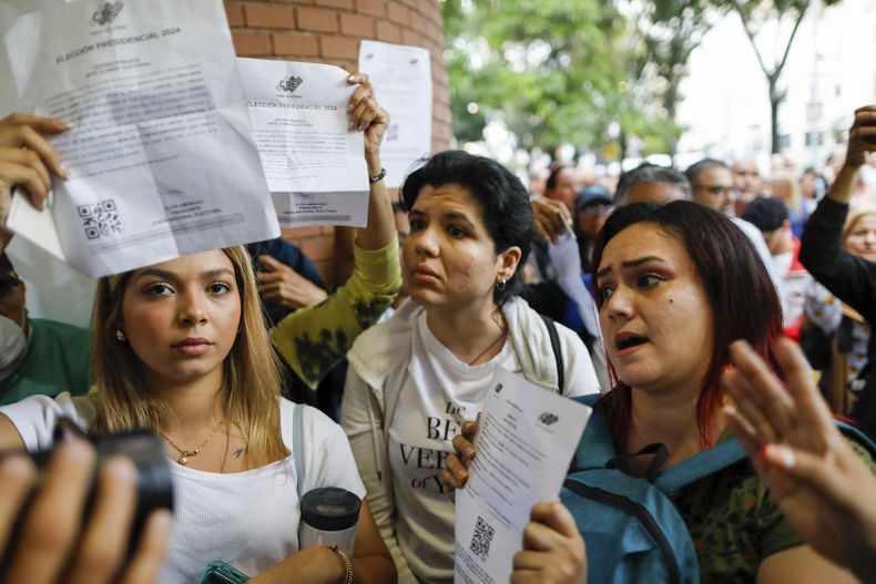 Los observadores electorales de la oposición exhiben documentos que los identifican como tales en la entrada de la Escuela Andrés Bello, el principal colegio electoral de Caracas, Venezuela, durante las elecciones presidenciales del domingo 28 de julio de 2024. (AP Foto/Cristian Hernández)