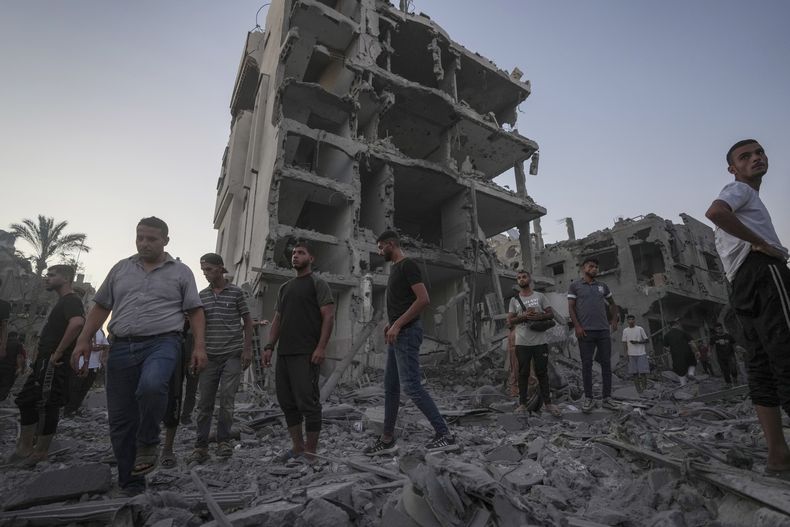 Palestinos caminan sobre los escombros dejados por un bombardeo israelí contra en Deir al Balah, en la Franja de Gaza, el martes 6 de agosto de 2024. (AP Foto/Abdel Kareem Hana)
