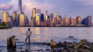 ARCHIVO - Un hombre comprueba dónde pisa mientras camina por el agua en el Canal Morris en Jersey, Nueva Jersey, mientras se pone el sol con Manhattan de fondo, el 31 de mayo de 2022. (AP Foto/J. David Ake, Archivo)