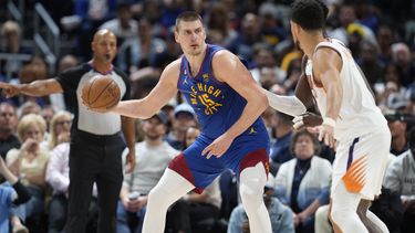 El serbio Nikola Jokic, de los Nuggets de Denver, busca enviar un pase frente a Devin Booker, de los Suns de Phoenix, en el encuentro de playoffs disputado el sábado 29 de abril de 2023 (AP Foto/David Zalubowski)