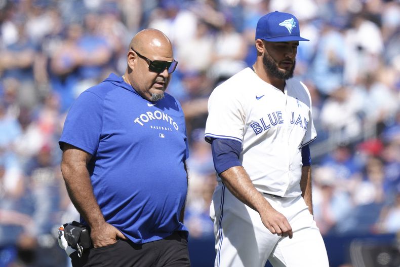 El lanzador relevista de los Azulejos de Toronto, Yimi García, a la derecha, camina de regreso al dugout con un miembro del personal médico de los Azulejos durante la novena entrada contra los Guardianes de Cleveland en Toronto, el domingo 16 de junio de 2024. (Chris Young/The Canadian Press vía AP)