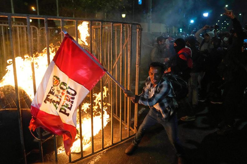 ARCHIVO - Un manifestante ondea una bandera peruana mientras una muñeca de cartón arde frente al Congreso durante una protesta contra el nuevo presidente José Jeri en Lima, Perú, el miércoles 15 de octubre de 2025. (AP Foto/Martín Mejía, Archivo)