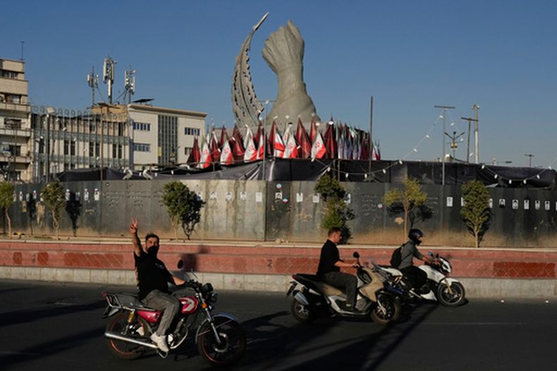 Un hombre hace un gesto a la cámara mientras pasa ante un monumento que representa el puño cerrado del fallecido líder supremo iraní Alí Jamenei, asesinado por ataques de Estados Unidos e Israel el 28 de febrero, y un misil, en la plaza de la Revolución Islámica en el centro de Teherán, Irán, el martes 15 de septiembre de 2026. (AP Foto/Vahid Salemi)