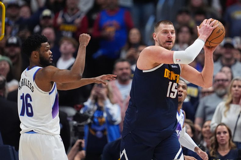 Nikola Jokić, derecha, de los Nuggets de Denver, busca a quien pasar el balón mientras Elijah Harkless, del Jazz de Utah, defiende durante la segunda mitad del juego de baloncesto de la NBA, el viernes 27 de marzo de 2026, en Denver. (AP Foto/David Zalubowski)