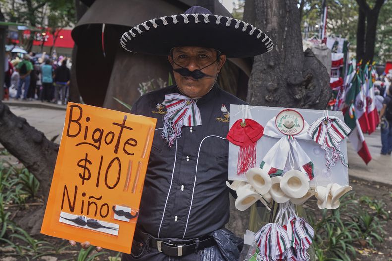 Un vendedor ofrece bigotes falsos y otras baratijas durante el desfile militar del Día de la Independencia en la Ciudad de México, el martes 16 de septiembre de 2025. (Foto AP/Jon Orbach)