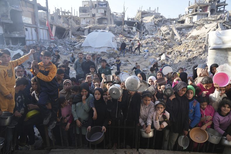 Niños y adultos palestinos esperan recibir alimentos donados en un centro de distribución en Beit Lahiya, en la Franja de Gaza, el domingo 16 de marzo de 2025. (AP Foto/Abdel Kareem Hana)