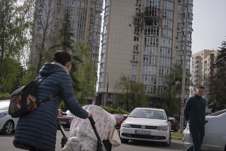 Gente pasa junto a un edificio de apartamentos dañado por restos de un dron derribado durante un ataque ruso la noche anterior en Kiev, Ucrania, el lunes 8 de mayo de 2023. (AP Foto/Andrew Kravchenko)