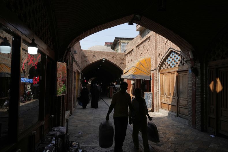 Dos personas cargan con bolsas de la compra por una calle del histórico vecindario de Oudlajan, en Teherán, Irán, el 31 de julio de 2025. (AP Foto/Vahid Salemi)