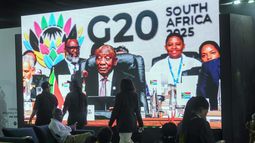 Gente pasa frente a un televisor gigante donde el presidente sudafricano Cyril Ramaphosa sostiene un mazo de madera cuando clausura oficialmente la cumbre de líderes del G20, en Johannesburgo, Sudáfrica, el domingo 23 de noviembre de 2025. (Foto AP/Jerome Delay)