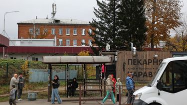 Varias personas en una parada de autobús en Shelekhov, en las afueras de Irkutsk, Rusia, el jueves 8 de octubre de 2026, con el hospital del distrito y el centro médico para el tratamiento de enfermedades infecciosas como fondo. (AP Foto)