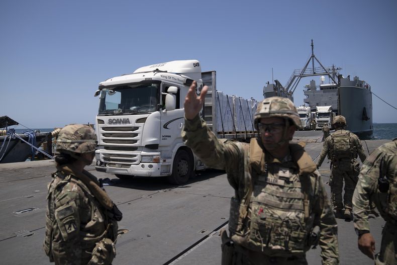 Un soldado del ejército de Estados Unidos hace señas al conductor de un camión cargado con asistencia humanitaria a su llegada al muelle flotante Trident, construido por Estados Unidos, antes de llegar a la playa en la costa de la Franja de Gaza, el martes 25 de junio de 2024. (AP Foto/Leo Correa)