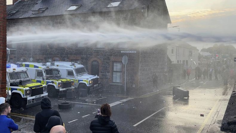 En este fotograma tomado de un video de PA, policías usan un cañón de agua cerca de Clonavon Terrace, en Ballymena, Irlanda del Norte, mientras personas protestan por un presunto ataque sexual en el poblado del condado Antrim, el martes 10 de junio de 2025. (Niall Carson/PA vía AP)