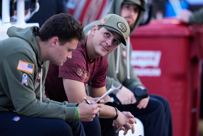 El quarterback lesionado de los 49ers de San Francisco, Brock Purdy, en el medio, se sienta en el banquillo durante la primera mitad de un juego de fútbol americano de la NFL contra los Rams de Los Ángeles en Santa Clara, California, el domingo 9 de noviembre de 2025. (AP Photo/Godofredo A. Vásquez)