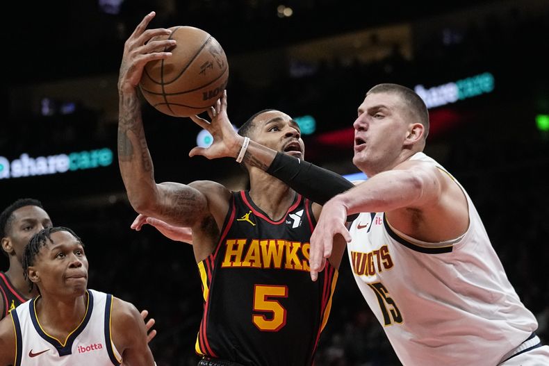 Dejounte Murray (5), de los Hawks de Atlanta, reta la marca defensiva de Nikola Jokic (15), de los Nuggets de Denver, durante la primera mitad del juego de baloncesto de la NBA, el lunes 11 de diciembre de 2023, en Atlanta. (AP Foto/John/Bazemore)