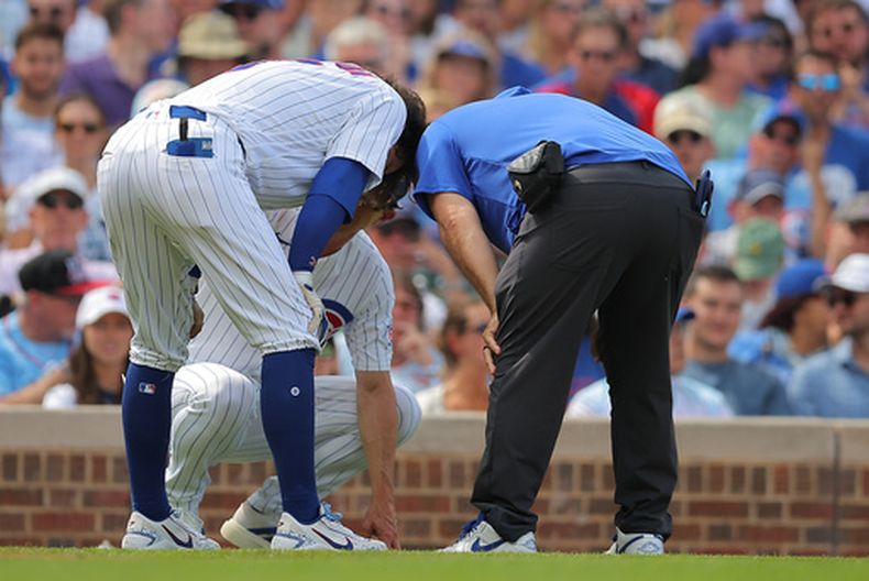 Dansby Swanson, de los Cachorros de Chicago, (al frente izquierda) se dobla del dolor tras lastimarse durante su turno al bat al tiempo que el mánager Craig Counsell, (abajo izquierda), lo revisa junto a un preparador físico, (derecha) durante la tercera entrada de un juego de béisbol contra los Cardenales de San Luis, domingo 16 de agosto de 2026, en Chicago. (AP Foto/Melissa Tamez)