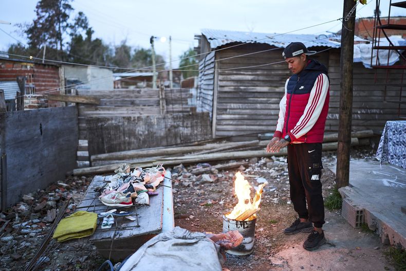 ARCHIVO - Tomás Vera calienta sus manos en un fuego afuera de su casa en el barrio de Garrote de Buenos Aires, Argentina, el martes 3 de junio de 2025. (AP Foto/Rodrigo Abd, Archivo)