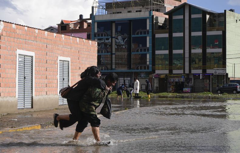La gente cruza una calle inundada después de fuertes lluvias en El Alto, Bolivia, el domingo 23 de marzo de 2025. (AP Foto/Juan Karita)