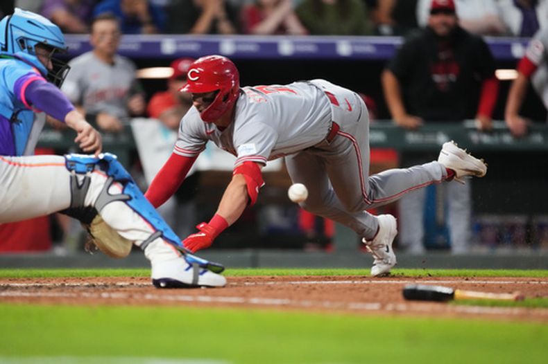 El receptor de los Rockies de Colorado, Hunter Goodman (izquierda), fildea el tiro mientras Spencer Steer, de los Rojos de Cincinnati, se desliza a salvo en el plato para apuntarse un jonrón dentro del parque ante el lanzador relevista de Colorado, Jeff Criswell, en la octava entrada de un partido de béisbol el viernes 17 de julio de 2026, en Denver. (Foto AP/David Zalubowski)