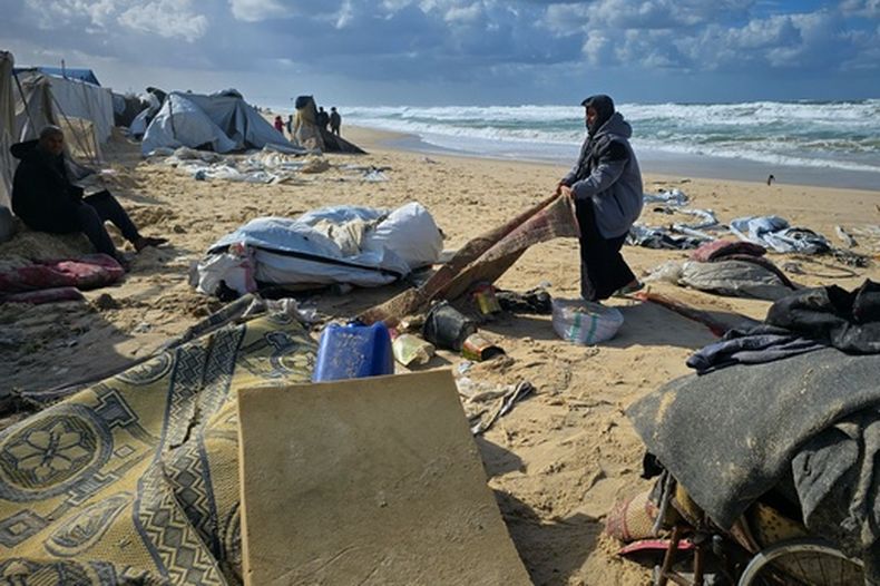 Una mujer jala una alfombra después de que lluvias nocturnas inundaran un campamento de tiendas de campaña junto a la playa, el domingo 28 de diciembre de 2025, en Jan Yunis, en el sur de la Franja de Gaza. (AP Foto/Mohammad Jahjouh)