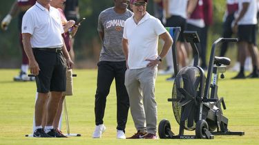 Josh Harris, derecha, nuevo dueño de los Commanders de Washington, sonríe con el legendario Joe Theismann, izquierda, Mitchell Rales, y otros, durante el entrenamiento del equipo en las instalaciones, el miércoles 26 de julio de 2023, en Ashburn, Virginia. (AP Foto/Alex Brandon)