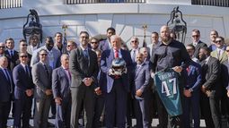 El tackle ofensivo de los Eagles de Filadelfia Lane Johnson junto al entrenador Nick Sirianni y al presidente de los Estados Unidos, quien sostiene un casco durante la visita de los campeones defensores del Super Bowl a la Casa Blanca el lunes 28 de abril del 2025. (AP Foto/Mark Schiefelbein)