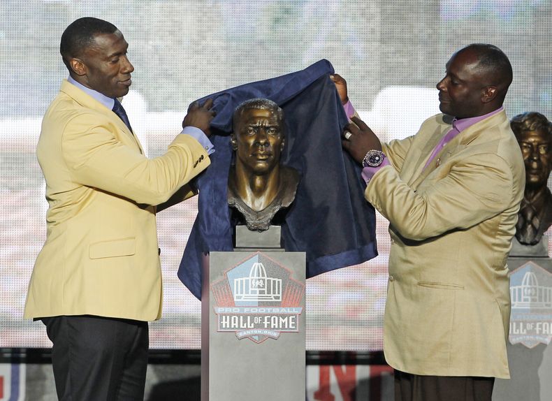 ARCHIVO - Foto del 6 de agosto del 2011, Shannon Sharpe devela el busto con su imagen junto a su hermano Sterling Sharpe durante su inducción al Salón de la Fama. (AP Foto/Ron Schwane, Archivo)