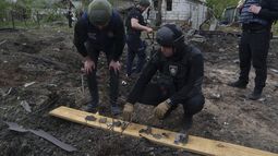 Un policía ucraniano y un fiscal de crímenes de guerra analizan fragmentos de una bomba frente a una residencia dañada después de un ataque aéreo ruso contra un vecindario residencial, el sábado 18 de mayo de 2024, en Járkiv, Ucrania. (AP Foto/Evgeniy Maloletka)