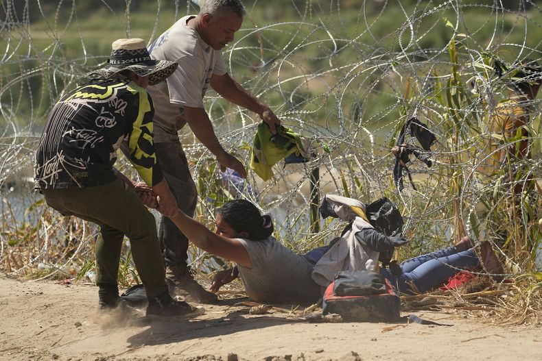 Una inmigrante que cruzó a Estados Unidos desde México es auxiliada a pasar debajo de alambre de púas en una de las márgenes del río Bravo, el jueves 21 de septiembre de 2023, en Eagle Pass, Texas. (AP Foto/Eric Gay)
