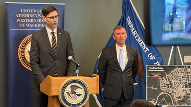 En esta foto tomada con un teléfono, Mike Herrington, el agente especial del FBI a cargo del caso, habla con los medios de comunicación mientras el fiscal federal interino Neil Floyd, a la derecha, escucha, el martes 6 de octubre de 2026, en Seattle. (AP Foto/Manuel Valdés)