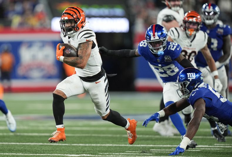 Chase Brown (30), running back de los Bengals de Cincinnati, corre con el balón superando al cornerback CorDale Flott (28) y al linebacker Bobby Okereke (58), de los Giants de Nueva York, para un touchdown durante la segunda mitad del juego de la NFL, el domingo 13 de octubre de 2024, en East Rutherford, Nueva Jersey. (AP Foto/Frank Franklin II)