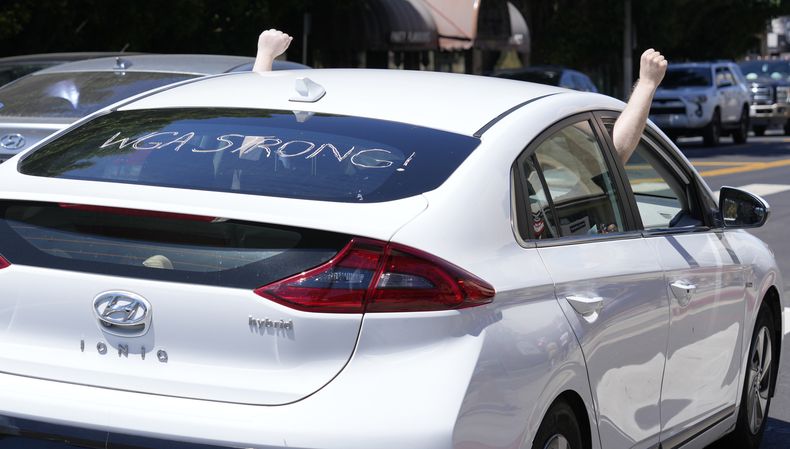 Un automóvil que dice en inglés fuerza WGA en el parabrisas trasero, en apoyo del Sindicato de Guionistas de Estados Unidos, pasa junto a escritores y actores en huelga fuera de los estudios Paramount en Los Ángeles el viernes 14 de julio de 2023. Los trabajadores están en huelga para obtener mejores salarios y condiciones de trabajo. (Foto AP/Chris Pizzello)
