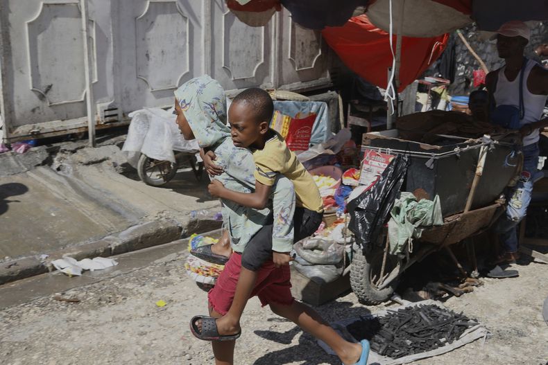 Un joven carga a un niño sobre su espalda en una escuela que actualmente sirve como albergue para quienes huyen de la violencia de las pandillas, el lunes 14 de abril de 2025, en Puerto Príncipe, Haití. (AP Foto/Odelyn Joseph)