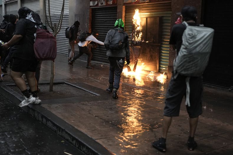Manifestantes intentan incendiar una tienda el 2 de octubre de 2023, luego de una marcha para conmemorar el 55º aniversario de los asesinatos de estudiantes que protestaban en la plaza de Tlatelolco, cuando soldados abrieron fuego sobre una manifestación pacífica, en la Ciudad de México. (AP Foto/Eduardo Verdugo)