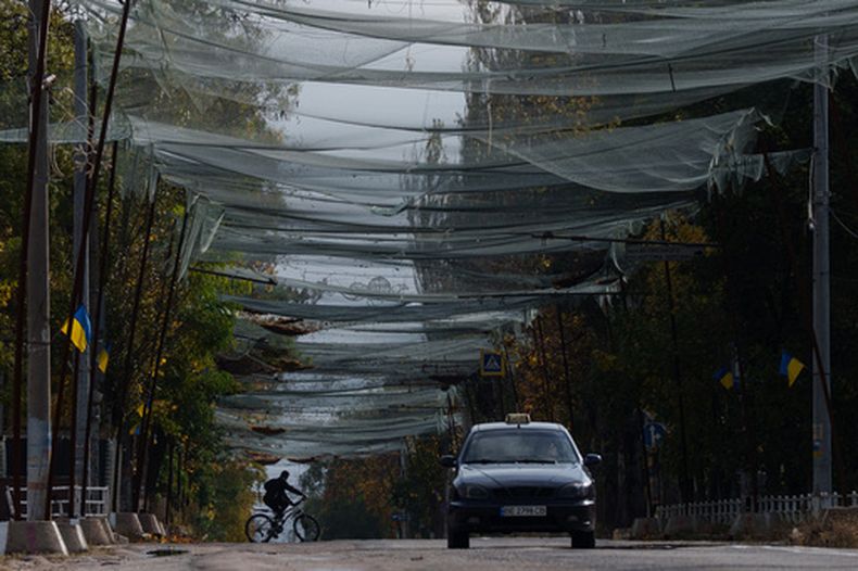 Un hombre monta en bicicleta bajo redes antidrones en una calle durante un cese el fuego asociado a una misión de paz en Oleshky, en Jersón, Ucrania, el miércoles 28 de octubre de 2026. (AP Foto/Evgeniy Maloletka)