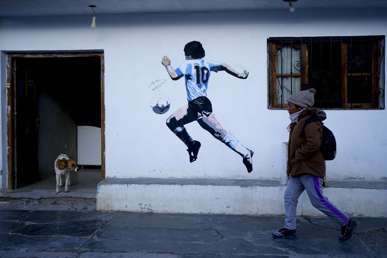 Una mujer camina por delante de un mural de la leyenda del fútbol argentino Diego Maradona, en San Antonio de los Cobres, Salta, Argentina, el martes 3 de octubre de 2023. (AP Foto/Natacha Pisarenko)