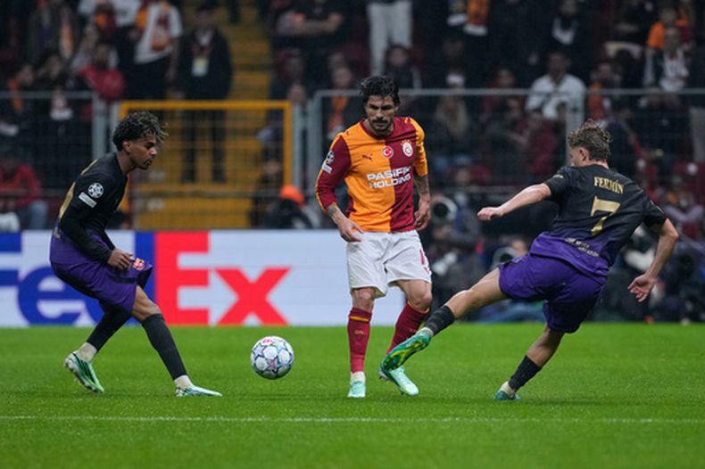 Eren Elmali (centro) de Galatasaray pugna por el balón con Lamine Yamal (izquierda) y Fermín López del Barcelona en el partido de la Liga de Campeones, el martes 13 de octubre de 2026, en Estambul. (AP Foto/Khalil Hamra)