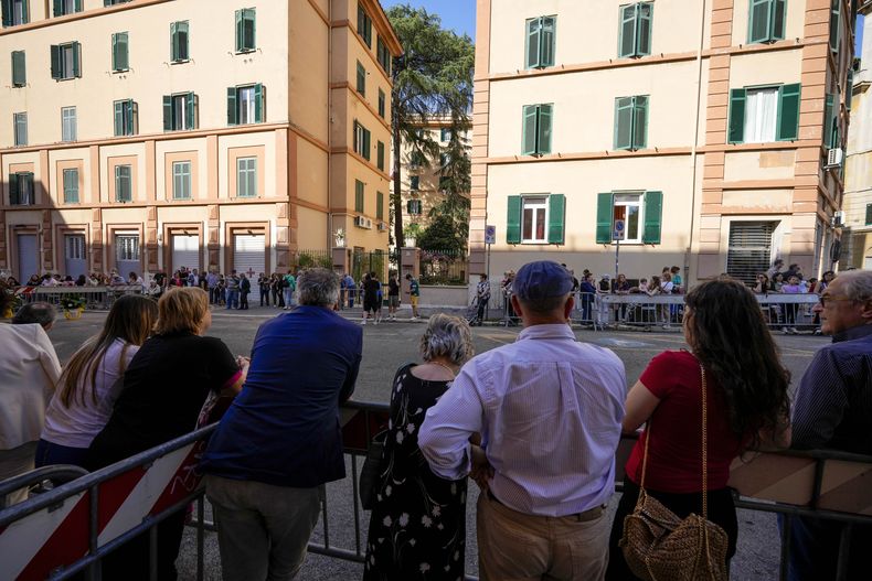 Un grupo de personas se reúne detrás de unas vallas frente a un bloque de apartamentos en Casal Bertone, en el extremo este de Roma, donde se esperaba la visita del papa Francisco, el jueves 6 de junio de 2024. (AP Photo/Andrew Medichini)