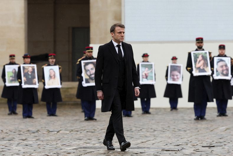 El presidente francés Emmanuel Macron camina frente a efectivos de la Guardia Republicana que sostienen retratos de las víctimas francesas del ataque de Hamás del 7 de octubre de 2023 en el monumento Invalides, París miércoles 7 de octubre de 2024. (Gonzalo Fuentes/Pool via AP)