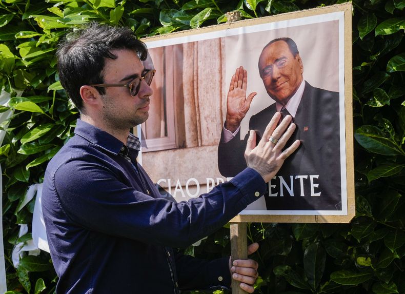 Un hombre se detiene frente a un cartel con la imagen de Silvio Berlusconi en las afueras de la residencia del fallecido ex primer ministro, en Arcore, cerca de Milán, el lunes 12 de junio de 2023. (AP Foto/Antonio Calanni)