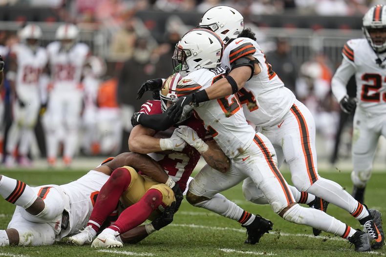 Christian McCaffrey, al centro, corredor de los 49ers de San Francisco, es derribado por varios jugadores de los Browns de Cleveland, entre ellos el ala defensivo Myles Garrett, izquierda, el safety Grant Delpit y el linebacker Sione Takitaki durante la segunda mitad del juego de la NFL, el domingo 15 de octubre de 2023, en Cleveland. (AP Foto/Sue Ogrocki)