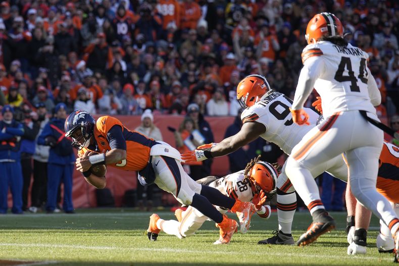Russell Wilson, izquierda, quarterback de los Broncos de Denver, anota un touchdown, superando a los defensivos de los Browns de Cleveland, el cornerback Mike Ford (28), el defensive tackle Dalvin Tomlinson (94) y el linebacker Sione Takitaki (44) durante la primera mitad del juego de la NFL el domingo 26 de noviembre de 2023, en Denver. (AP Foto/David Zalubowski)