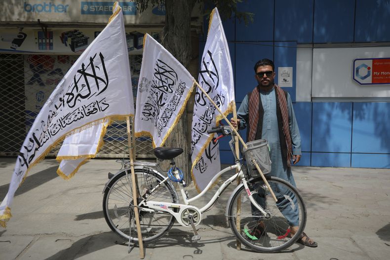 Un hombre posa para la cámara junto a su bicicleta, en la que vende banderas talibanes, antes de la celebración del 4to aniversario de la retirada de las tropas de EEUU del país y del inicio del gobierno del Talibán, en Kabul, el 14 de agosto de 2025. (AP Foto/Siddiqullah Alizai)