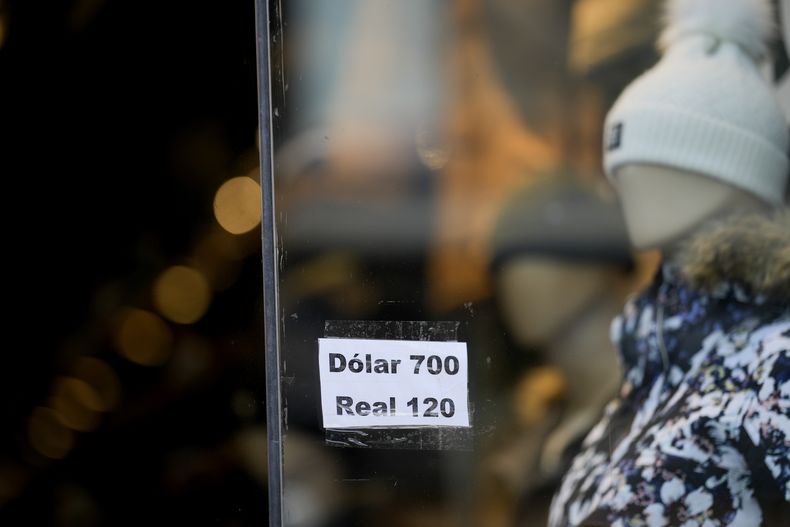 Una tienda de ropa con un cartel sobre el cambio oficial entre el dólar estadounidense y el real brasileño, ante el peso argentino, en Buenos Aires, Argentina, el lunes 14 de agosto de 2023. El peso argentino se hundió el lunes después de que el candidato ultraderechista resultara el más votado en las elecciones primarias en las que se eligieron los candidatos a presidente. (AP Foto/Natacha Pisarenko)