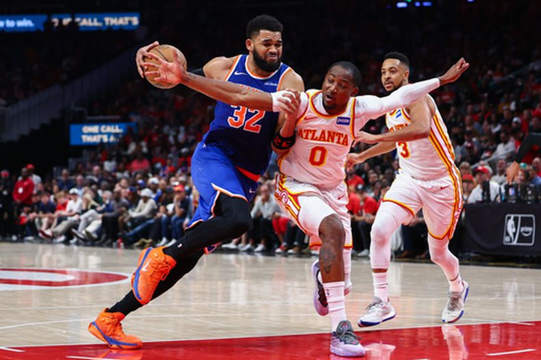 El centro de los Knicks de Nueva York, Karl-Anthony Towns (32), se dirige a la canasta contra el delantero de los Hawks de Atlanta, Jonathan Kuminga (0), durante la segunda mitad del tercer juego de una serie de playoffs de baloncesto de la NBA de primera ronda, el jueves 23 de abril de 2026, en Atlanta. (AP Foto/Colin Hubbard)