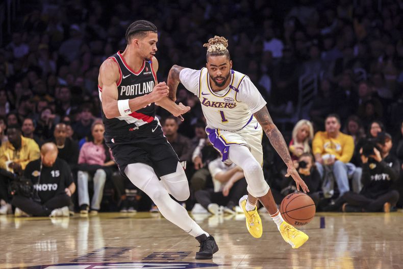 El base de los Lakers de Los Ángeles DAngelo Russell driblea el balón intentando superar al alero de los Trail Blazers de Portland Toumani Camara el domingo 8 de diciembre del 2024. (AP Foto/Etienne Laurent)