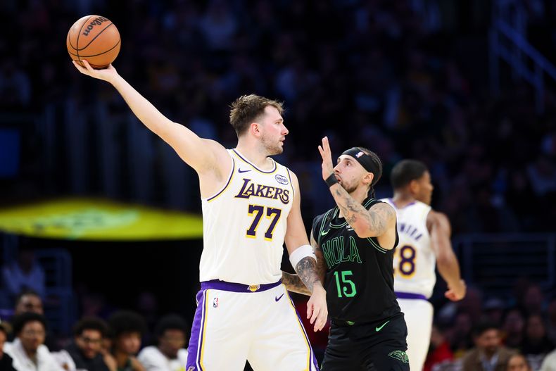 Luka Doncic (77), de los Lakers de Los Ángeles, sostiene el balón lejos de Jose Alvarado (15), de los Pelicans de Nueva Orleans, mientras Rui Hachimura, al fondo, corre durante la primera mitad del juego de baloncesto de la NBA, el domingo 30 de noviembre de 2025, en Los Ángeles. (AP Foto/Jessie Alcheh)