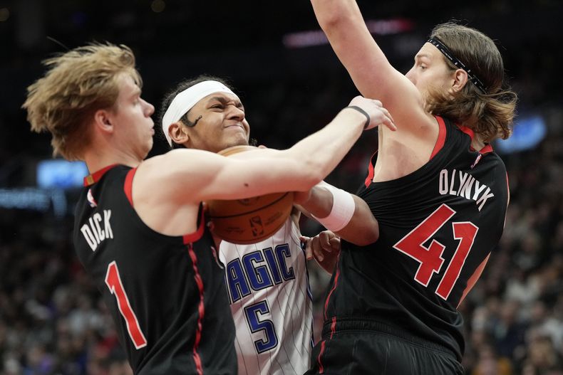 Paolo Banchero (5), del Magic de Orlando, trata de pasar entre Gradey Dick (1) y Kelly Olynyk (41), de los Raptors de Toronto, durante la segunda mitad del juego de baloncesto de la NBA, el viernes 15 de marzo de 2024, en Toronto. (Frank Gunn/The Canadian Press via AP)