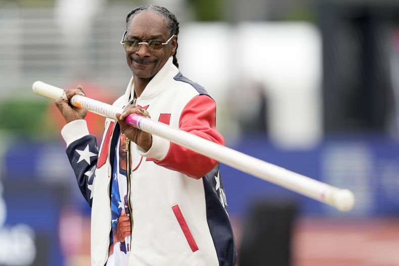 ARCHIVO - Snoop Dogg recibe una lección de salto con garrocha durante las pruebas por equipos olímpicos de atletismo de EE. UU. el 23 de junio de 2024, en Eugene, Oregón. Snoop fue uno de los últimos portadores de la antorcha olímpica antes de la ceremonia de apertura de los Juegos el viernes 26 de julio. (Foto AP/Charlie Neibergall, archivo)
