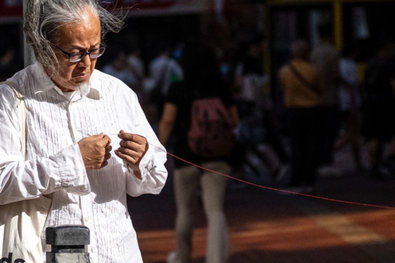 El artista Sanmu Chen sostiene un hilo rojo mientras actúa en la calle en la zona de Causeway Bay, Hong Kong, el 3 de junio de 2026, la víspera del 37mo aniversario de la represión en la plaza china de Tiananmen. (AP Foto/Chan Long Hei)