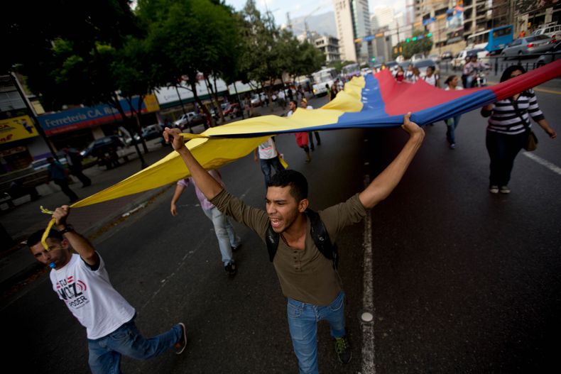 Estudiantes gritan consignas contra el presidente venezolano Nicol&aacute;s Maduro mientras ondean una bandera nacional, en Caracas, el viernes 25 abril de 2014. (Foto AP/Fernando Llano)